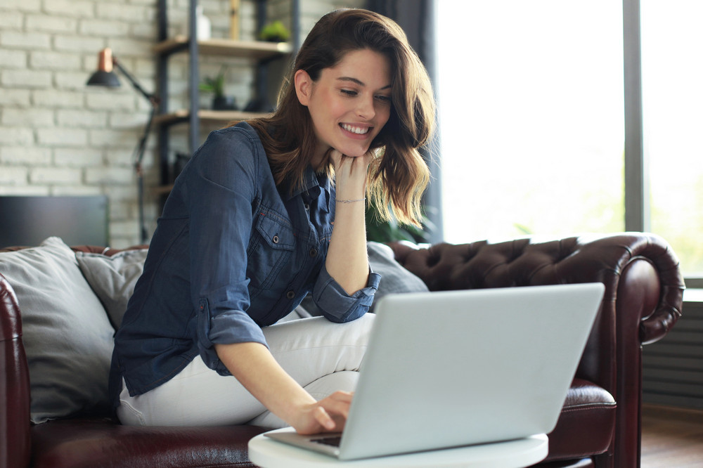 a young girl in a blue shirt smiles and works at a laptop