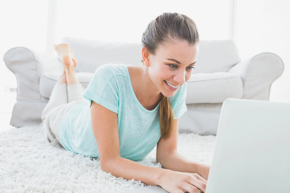 beautiful young girl in a white suit lying down working at a laptop
